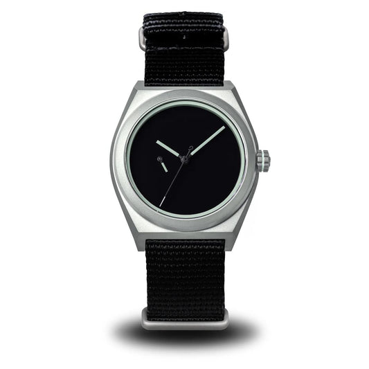 A minimalist wristwatch with a silver-toned metal case, black dial, and black woven fabric strap, shown against a plain white background. Boldr Venture Umbra