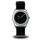 A minimalist wristwatch with a silver-toned metal case, black dial, and black woven fabric strap, shown against a plain white background. Boldr Venture Umbra